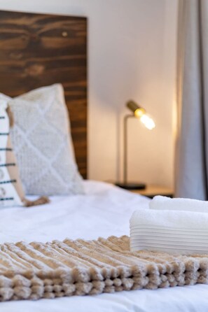 A neatly made bed with a folded white towel, a textured beige blanket, and a wooden headboard. - Studio Apartment in Colourful Bo-kaap (Cape Town)