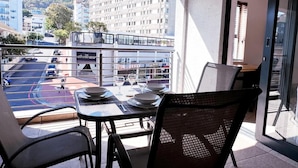 A balcony with a table set for two, overlooking a street with cars and buildings. - Spacious 1 Bedroom Apartment Atlantica Seapoint (Cape Town)