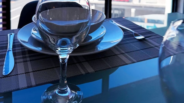 A table with a wine glass, a plate, and cutlery, set against a window with a view of buildings and a mountain. - Spacious 1 Bedroom Apartment Atlantica Seapoint (Cape Town)