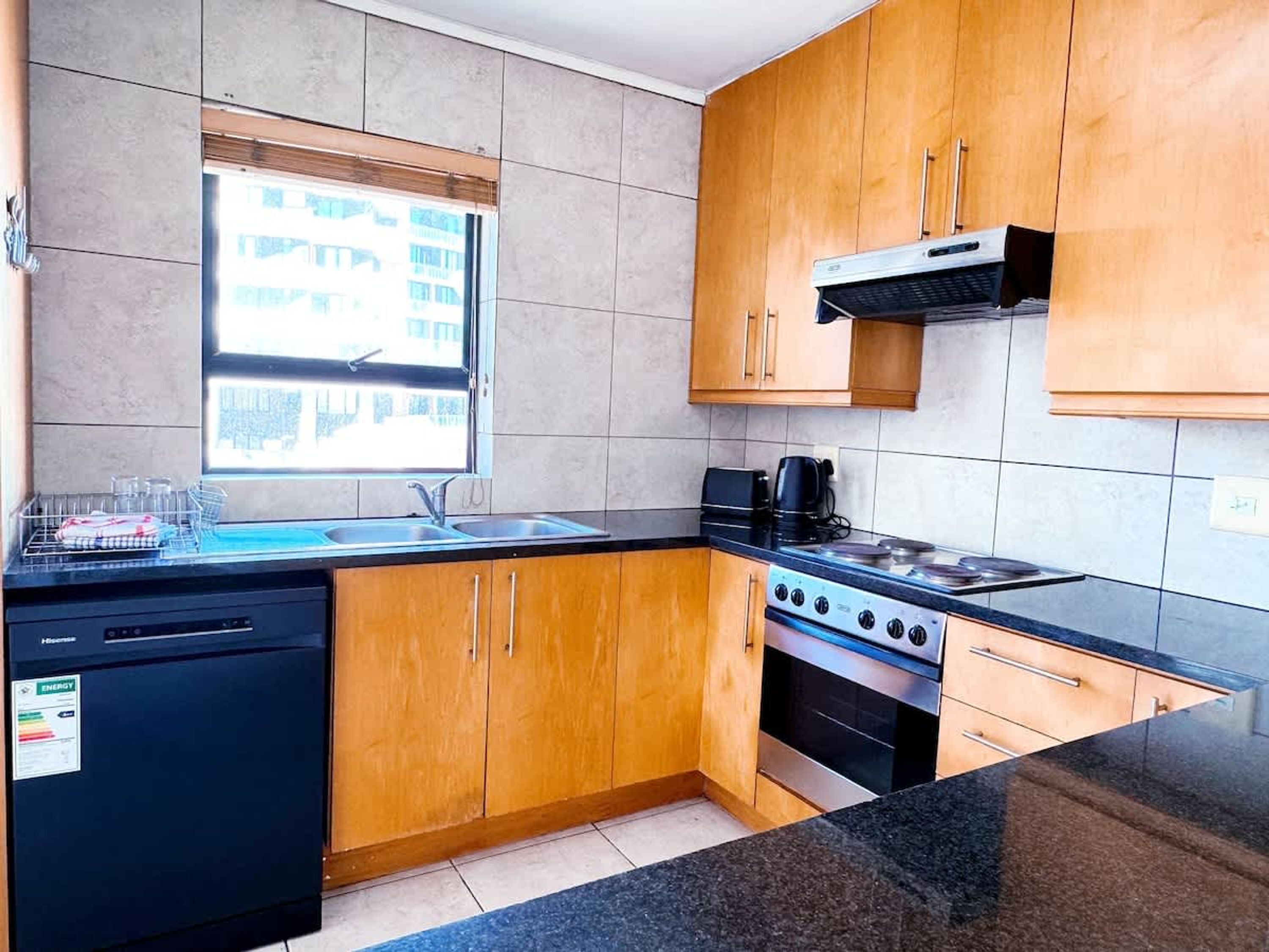 A compact kitchen with wooden cabinets, a gas stove, a dishwasher, and a window providing natural light.