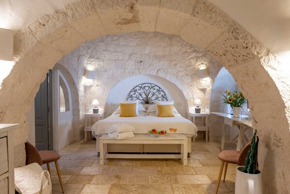 A bedroom with a stone arch, a bed with yellow pillows, bedside tables with lamps, and a bench with towels. - Casa Badra by Boutique (Martina Franca)