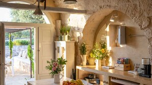 A rustic kitchen with stone walls, wooden furniture, and a fruit bowl on the table.