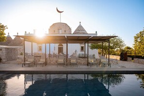 A poolside area with a covered seating area, stone walls, and a building with a dome and crescent. - Casa Badra by Boutique (Martina Franca)