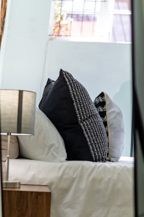 A neatly made bed with white bedding and several pillows, including a black one with a checkered pattern.
