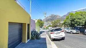 A street with parked cars, a yellow building, and mountains in the background.