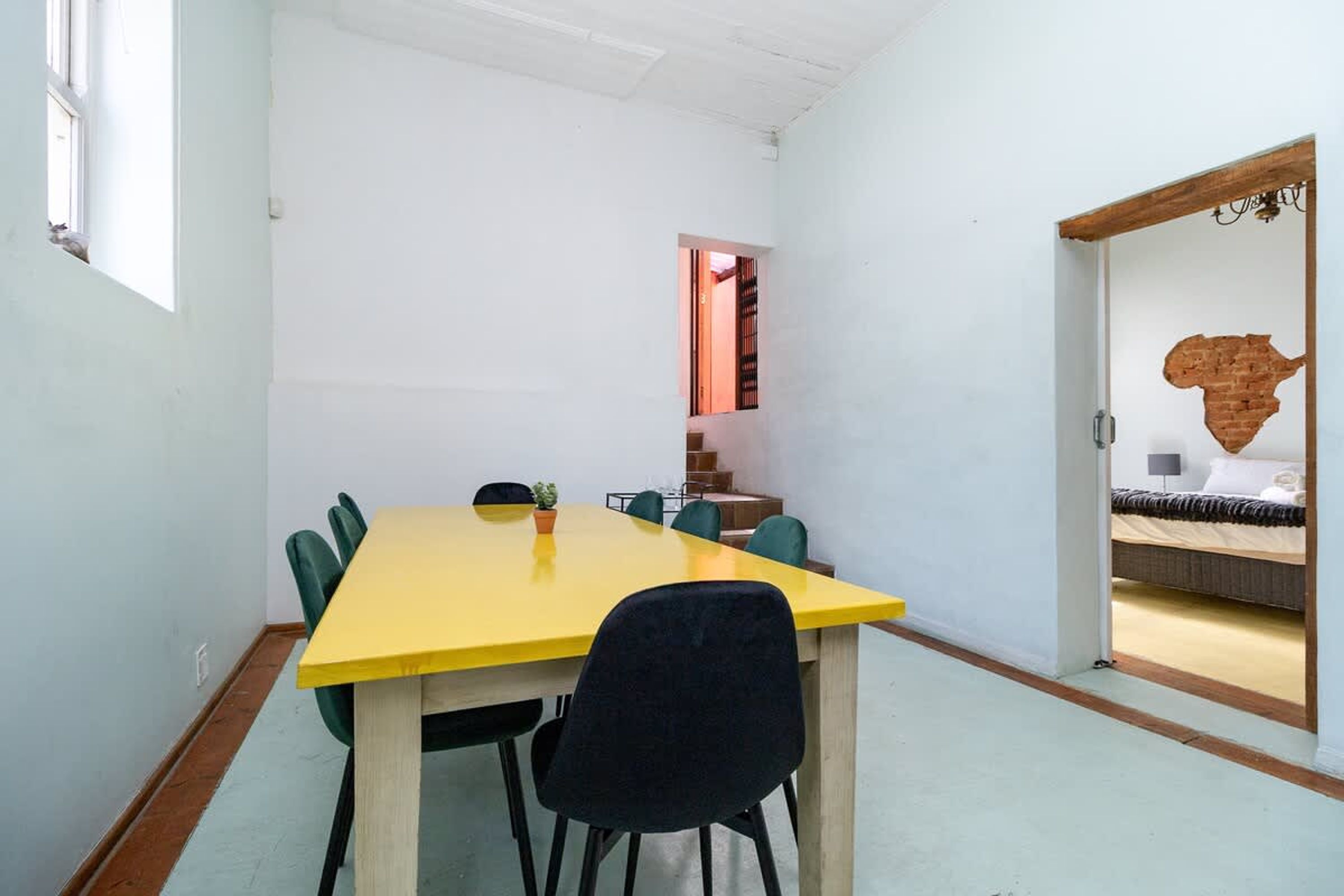 A room with a yellow table, black chairs, and a bed with a brick wall decoration.