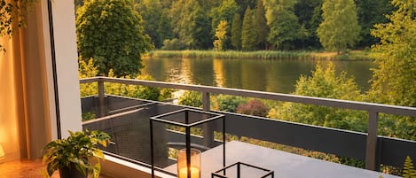 A balcony with a view of a lake and forest, a table with candles, and a potted plant.