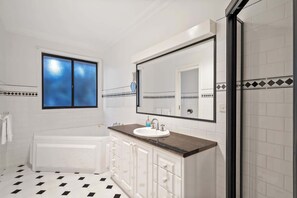 A bathroom with a white bathtub, a sink with a mirror above it, and a shower area. - Fairhaven (Mount Martha)