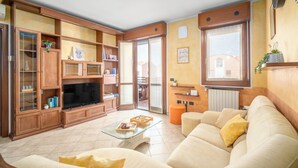 Sala de estar con sofá, mesa de centro, televisor, armarios de madera y puerta corrediza de vidrio que da a un balcón.