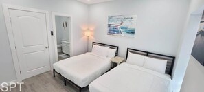 Una habitación de hotel con dos camas, una puerta, una lámpara y un cuadro en la pared.