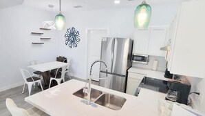 A modern kitchen with white cabinets, a stainless steel refrigerator, a built-in oven, and a dining area with a white table and chairs. - New 3BR Townhome | Pool | Sleeps 10 | 2 Levels (South Padre Island)