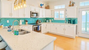 A kitchen with white cabinets, a stainless steel sink, a microwave, and a teal backsplash. - Luxury House w/ Private Pool I 2-Min Walk to Beach | Sleeps 16 (South Padre Island)