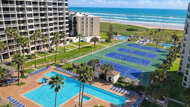 Un hotel con piscina, canchas de tenis y vista al mar.