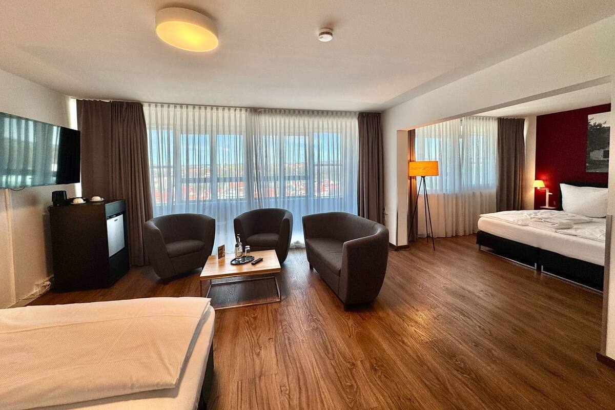 A hotel room with a bed, a desk, two armchairs, a coffee table, and a TV.