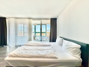 A hotel room with a large bed, a view of the city through the window, and a balcony with chairs. - My Park hotel Kempten by AR hotels (Kempten)