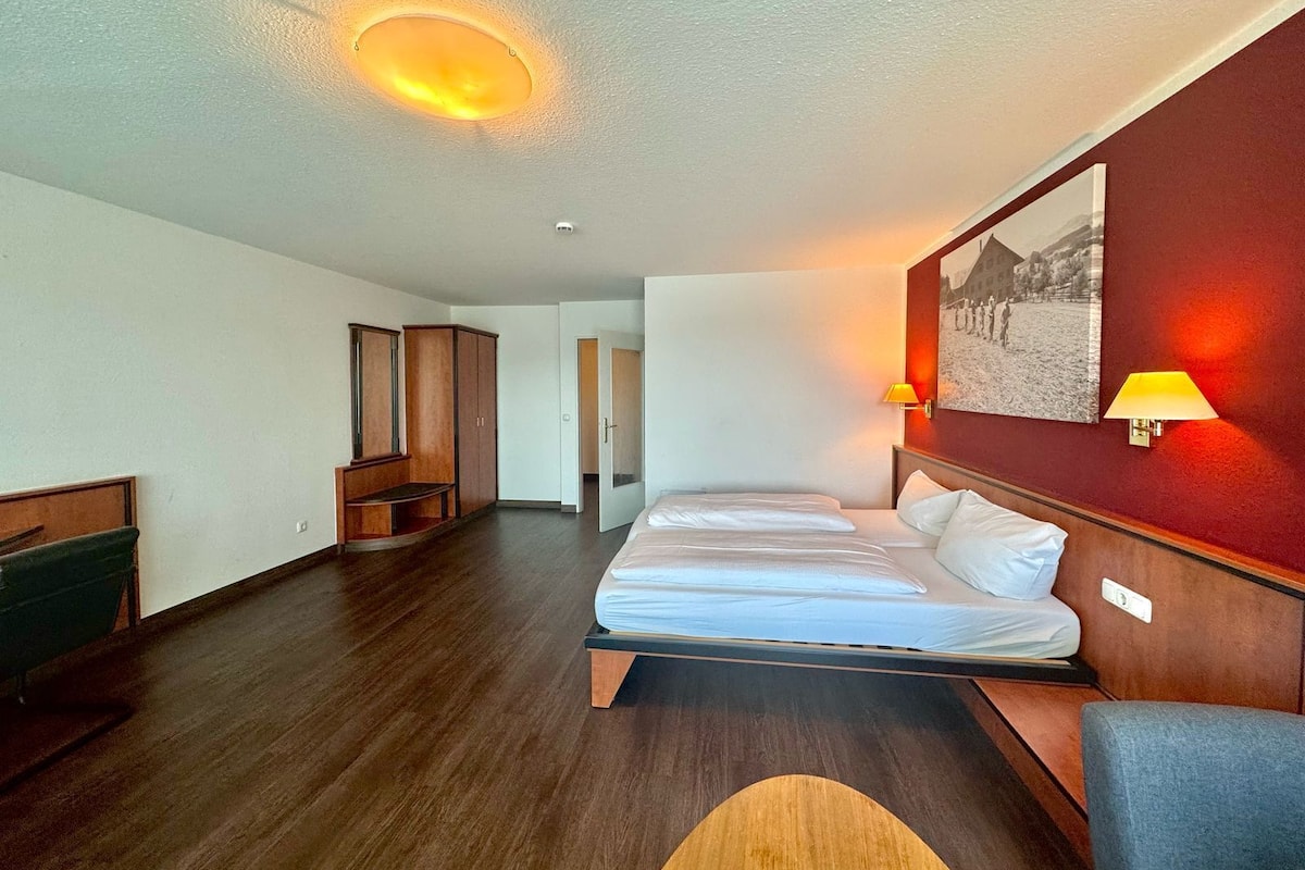 A hotel room with a large bed, wooden wardrobe, and a desk.
