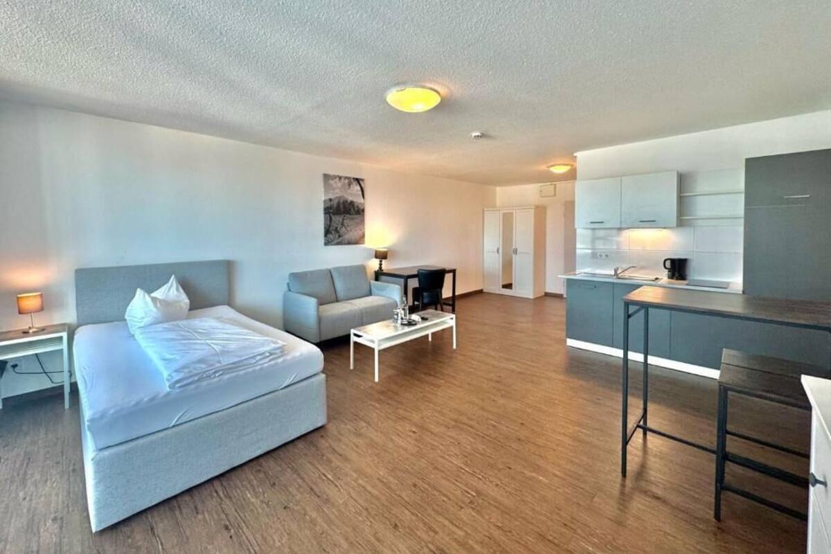 A modern apartment with a large bed, a sofa, a dining area, and a kitchen.