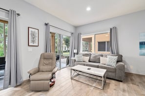 Un salon moderne comprenant un fauteuil inclinable, un canapé et une table basse, de grandes fenêtres et une porte-fenêtre coulissante.