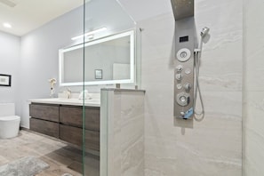 A modern bathroom with a glass shower enclosure, a large mirror, and a vanity with a sink and storage.