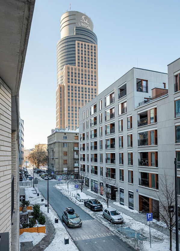 A modern urban street with snow on the ground, a tall building with the logo "UNIQA" in the background, and several parked cars.