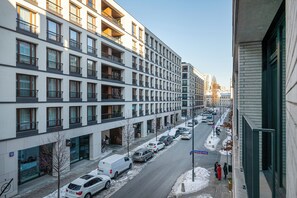 A multi-story residential building with balconies, parked cars, and a clear sky.