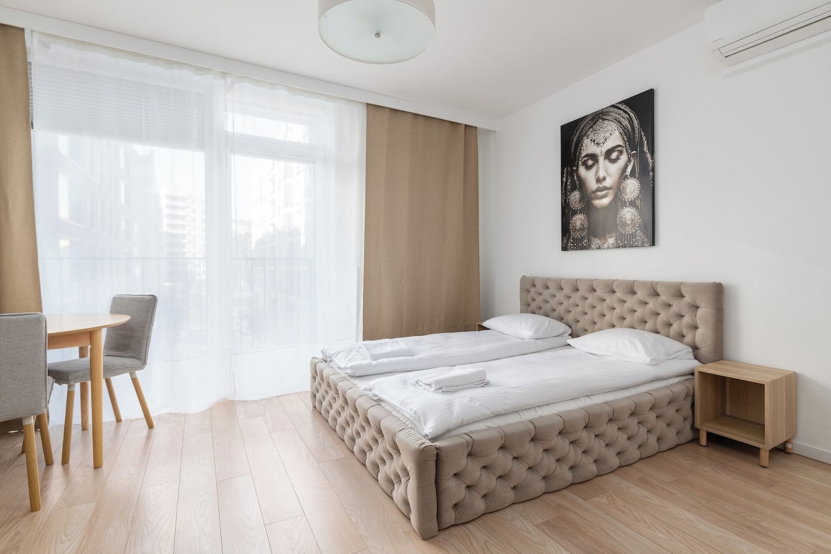Un dormitorio con una cama grande, una mesita de noche, una silla y una ventana con cortinas.