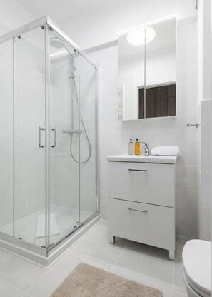 A modern bathroom with a glass-enclosed shower, a white vanity with a mirror, and a toilet.