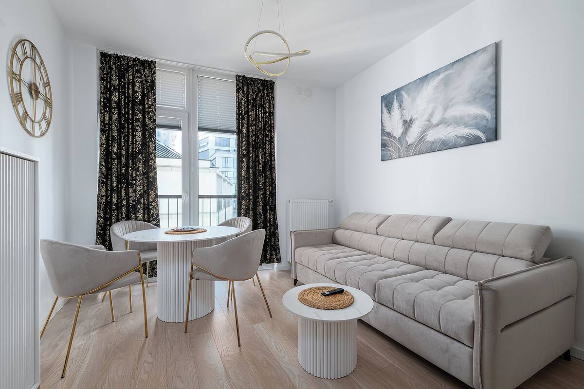 Una sala de estar moderna con un sofá beige, una mesa de comedor redonda con sillas y un cuadro abstracto grande en la pared.