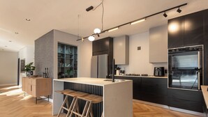 A modern kitchen with a central island, wooden stools, a built-in refrigerator, and a sleek black oven.