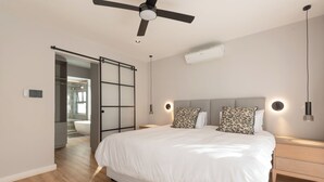 A modern bedroom with a large bed, a ceiling fan, bedside lamps, and a walk-in closet.