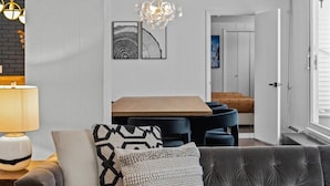 Een moderne woonkamer met een grijze bank, een houten eettafel en een kroonluchter.