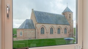 A view of a church with a clock tower and a smaller building, through a window with a picture frame and two glass candle holders. - Holiday Home in Zoutelande Near Sandy Beaches (Zoutelande)