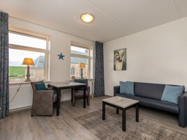 A room with a sofa, a table, a chair, and a lamp. There are windows with curtains and a star decoration on the wall.