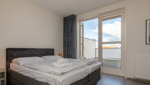 A modern bedroom with a large bed, a nightstand, a window with curtains, and a view of the sky. - Holiday Home in Zoutelande Near Sandy Beaches (Zoutelande)