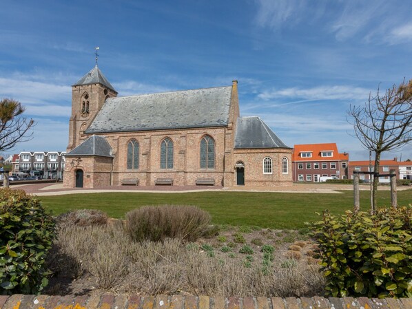 A church with a prominent tower and arched windows, surrounded by a well-maintained lawn and a brick wall. - Holiday Home in Zoutelande Near Sandy Beaches (Zoutelande)