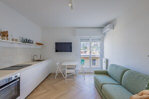 A modern kitchen with white cabinetry, a built-in oven, and a dining area with a white table and chairs. A green sofa is positioned near a sliding glass door leading to a balcony. - Goethe Charming Home by Wonderful Italy (Sanremo)