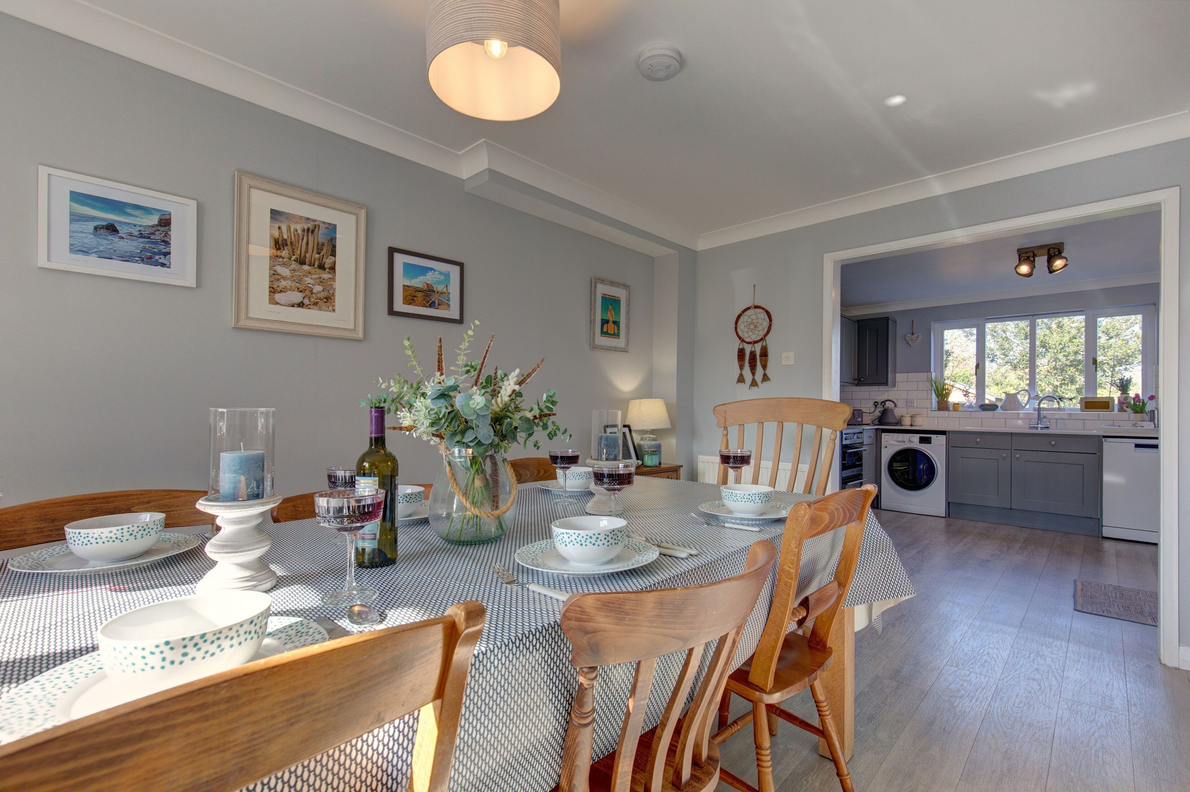 A dining area with a table set for four, surrounded by wooden chairs, and a kitchen visible in the background.