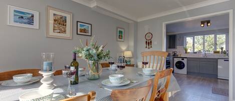 A dining area with a table set for four, surrounded by wooden chairs, and a kitchen visible in the background.