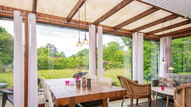 A wooden dining table with chairs, a sofa, and a view of a garden through large windows.