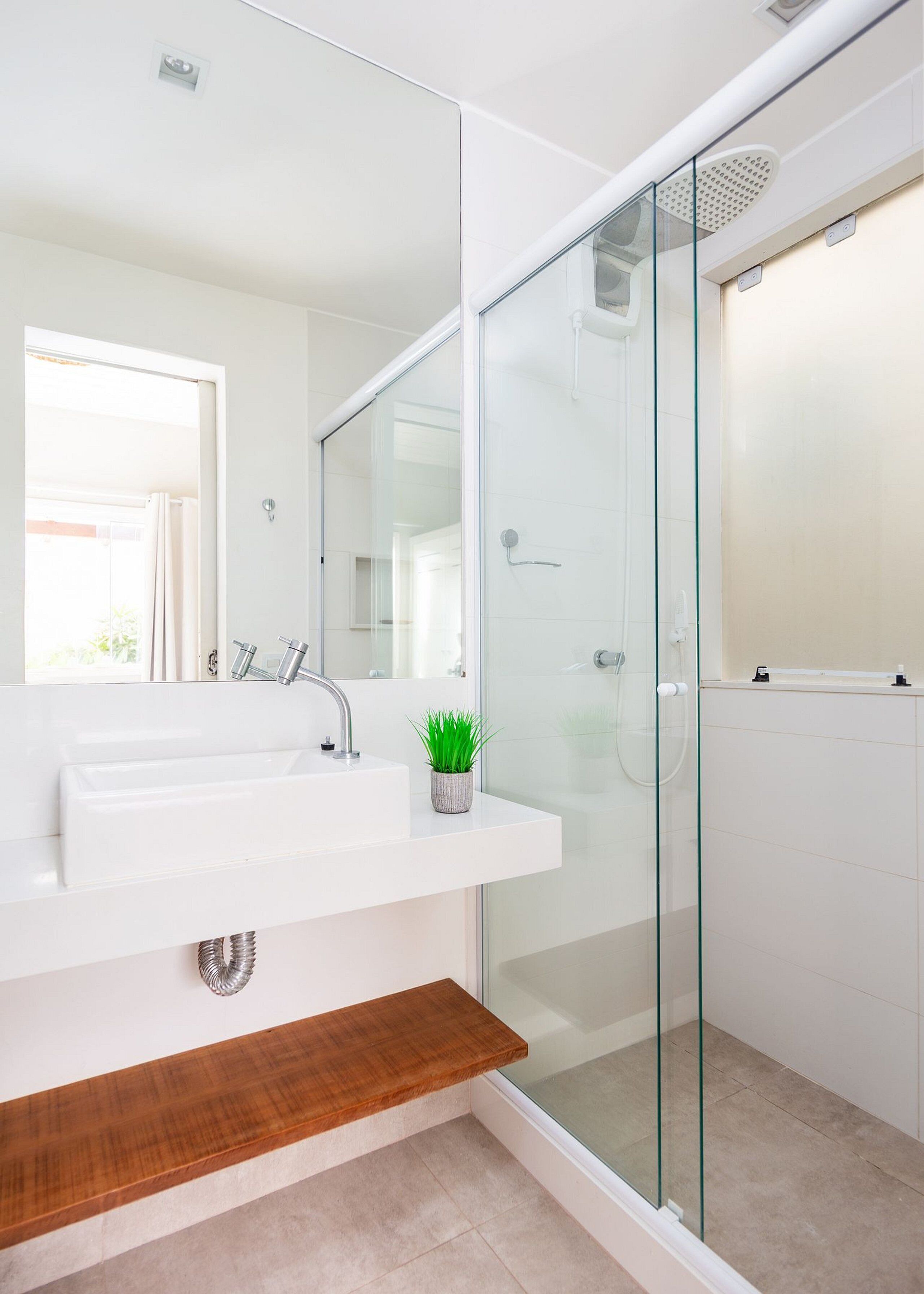 Un baño moderno con cabina de ducha de vidrio, un lavamanos blanco con espejo y una pequeña planta en maceta sobre el lavamanos.