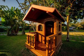 Una cabaña de madera con un porche y una ventana pequeña, rodeada de vegetación exuberante.
