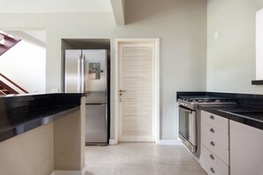 Una cocina con un refrigerador de acero inoxidable, una estufa y una puerta con persianas horizontales.