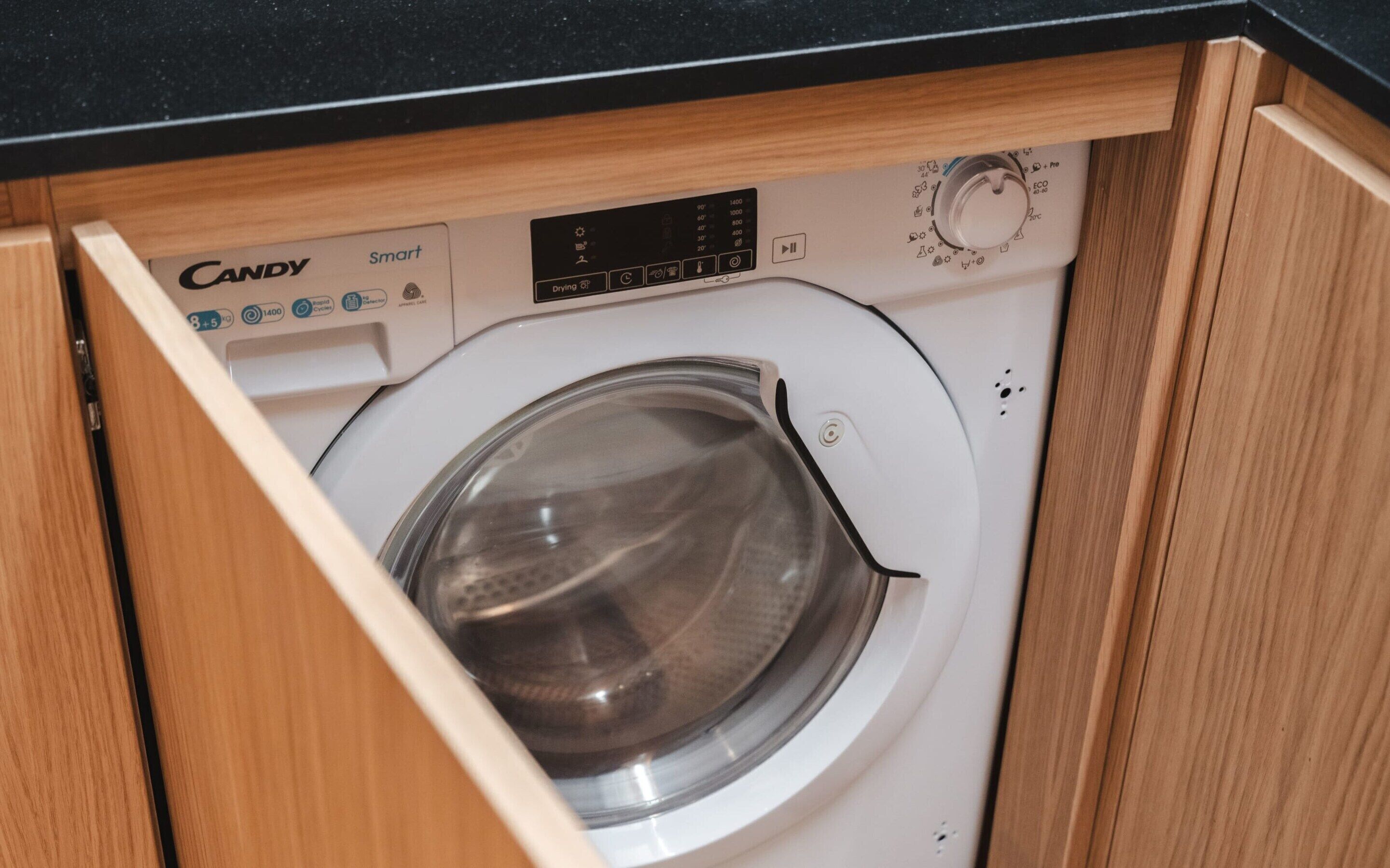 A Candy Smart washing machine in a wooden cabinet.