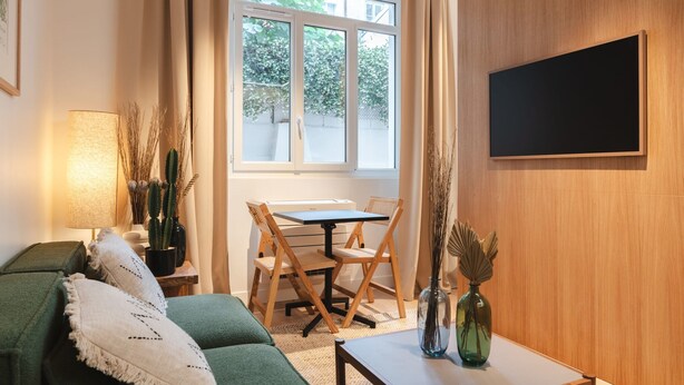 A cozy living room with a green sofa, a small table, and a TV mounted on the wall. - AC Apartment With Terrace in the Center of Paris (Paris)