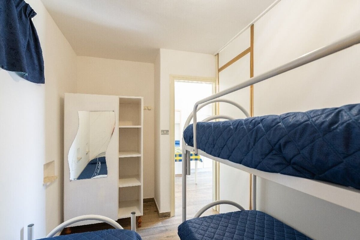A bunk bed room with a white metal ladder, a white wardrobe, and a mirror on the wall.