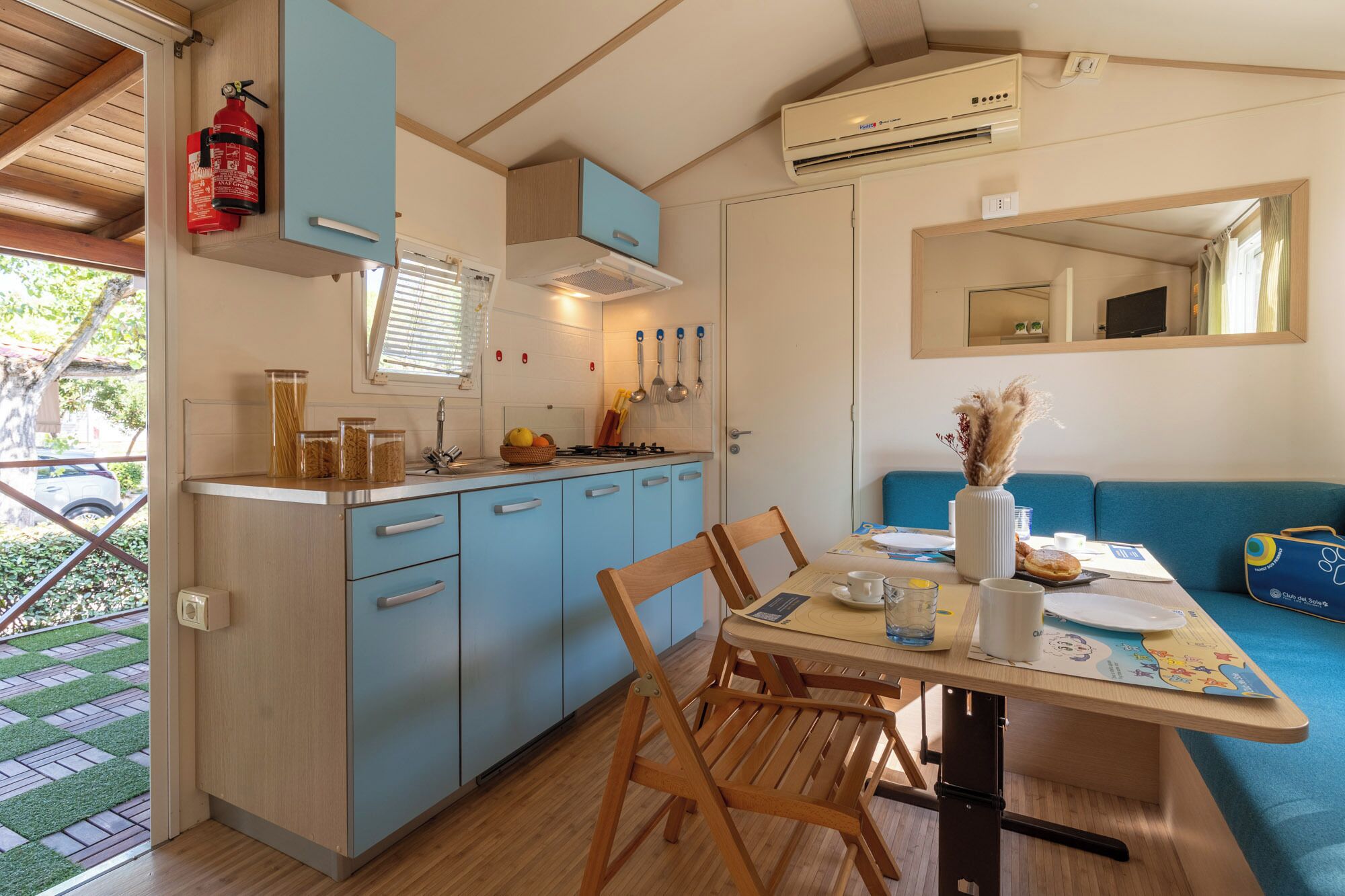 A compact kitchen with a sink, stove, and blue cabinets. There's a dining table with chairs and a blue sofa.