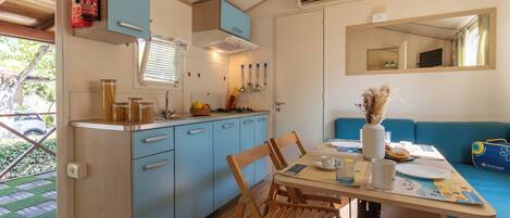 Cocina compacta con lavabo, estufa y armarios azules. Hay una mesa de comedor con sillas y un sofá azul.