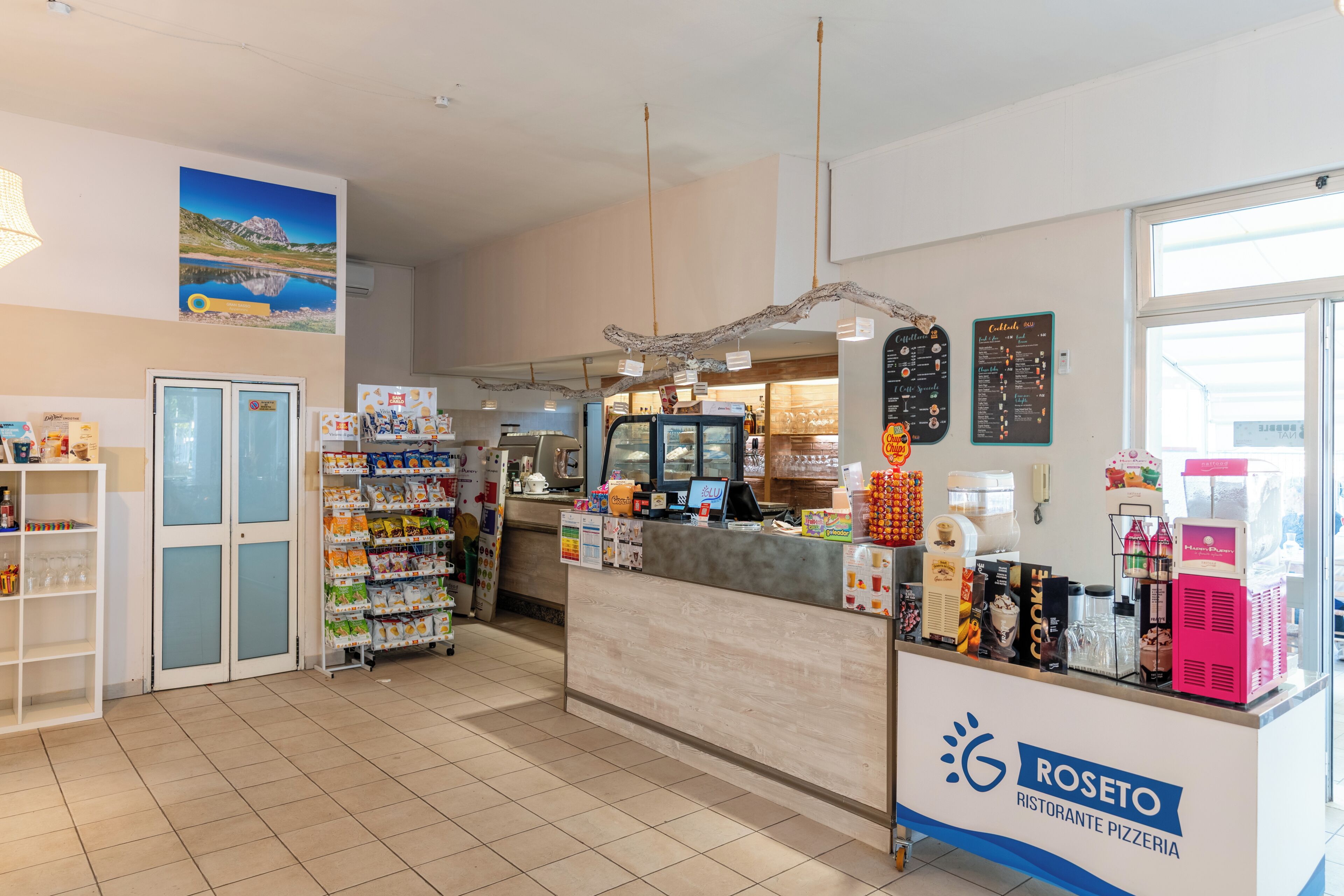 A pizzeria with a counter, refrigerated display, and a menu board.