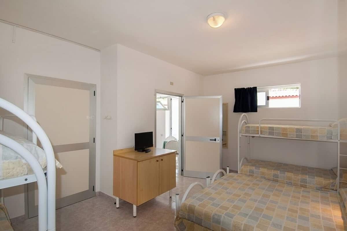 A bedroom with bunk beds, a wooden dresser, a television, and a window with curtains.