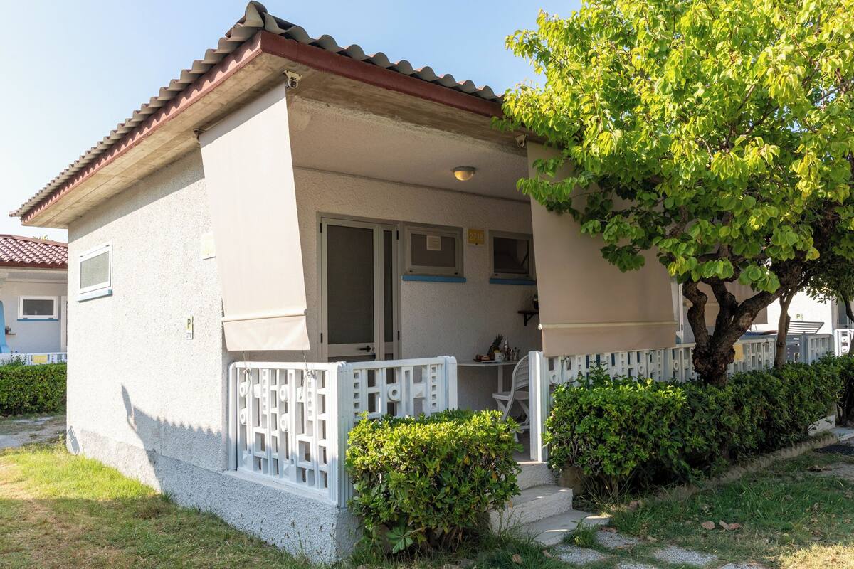 A small, single-story house with a tiled roof, a covered porch, and a small garden area.